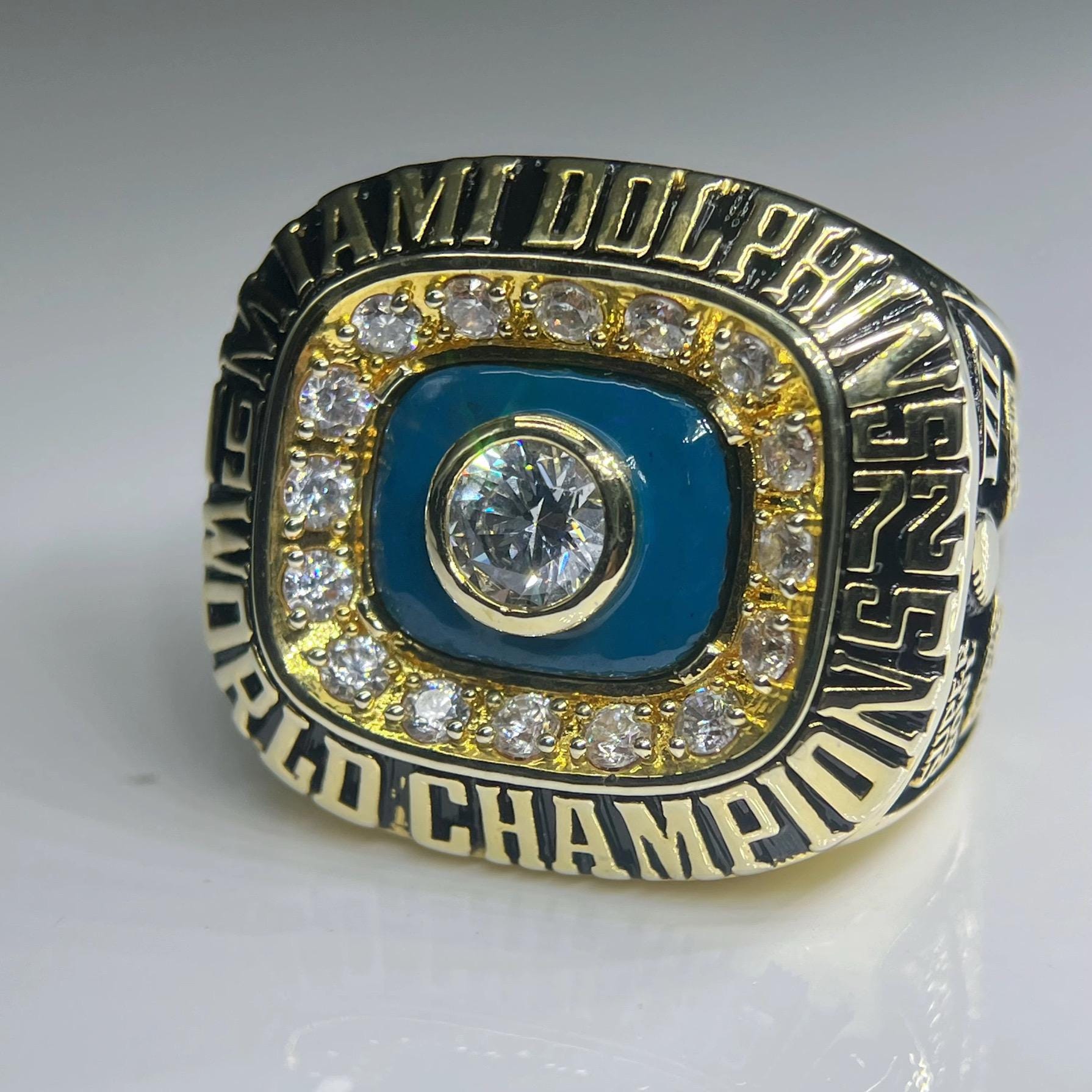 Gold and blue championship ring with engraved text on a gray background