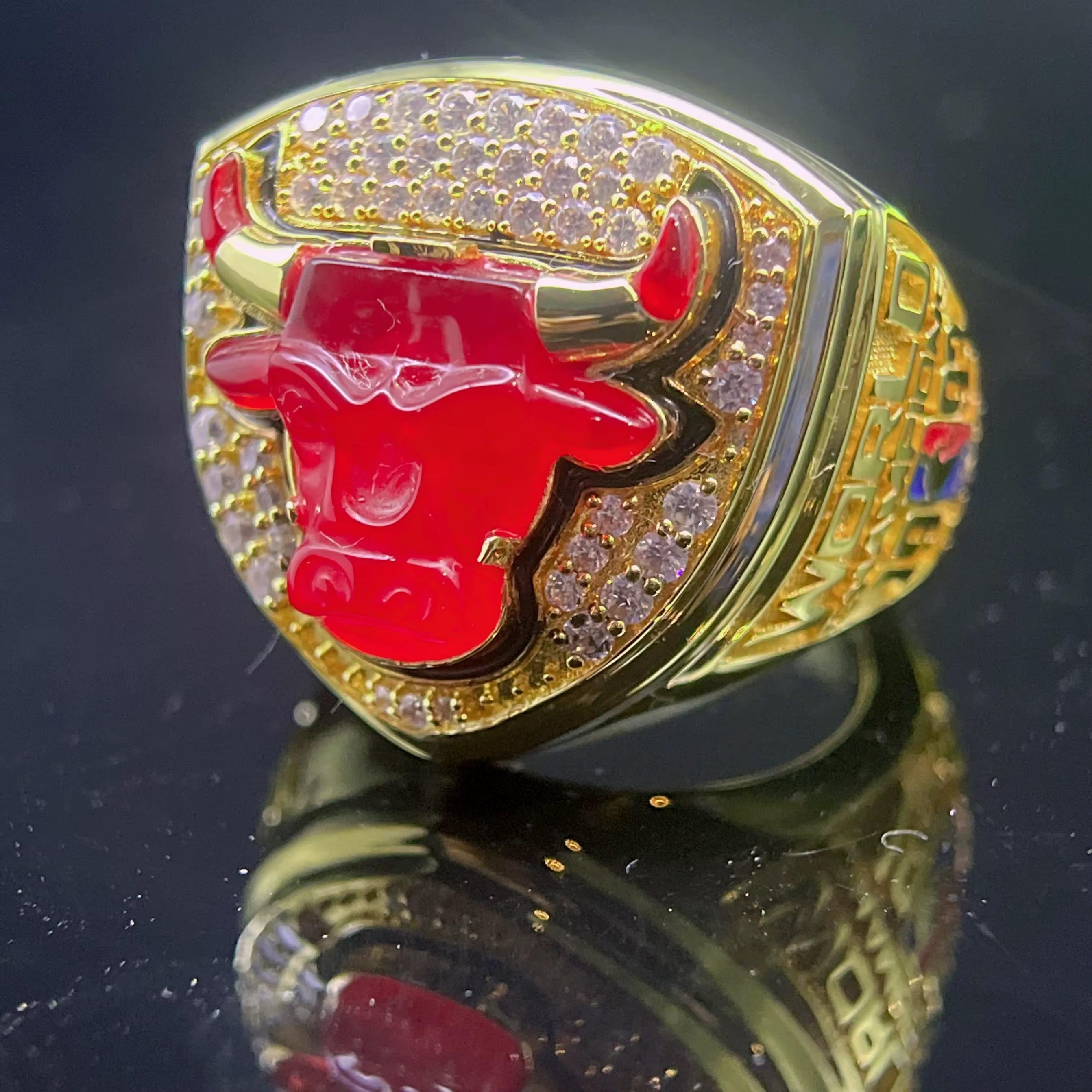 Gold ring with red bull emblem and gemstones on a reflective surface