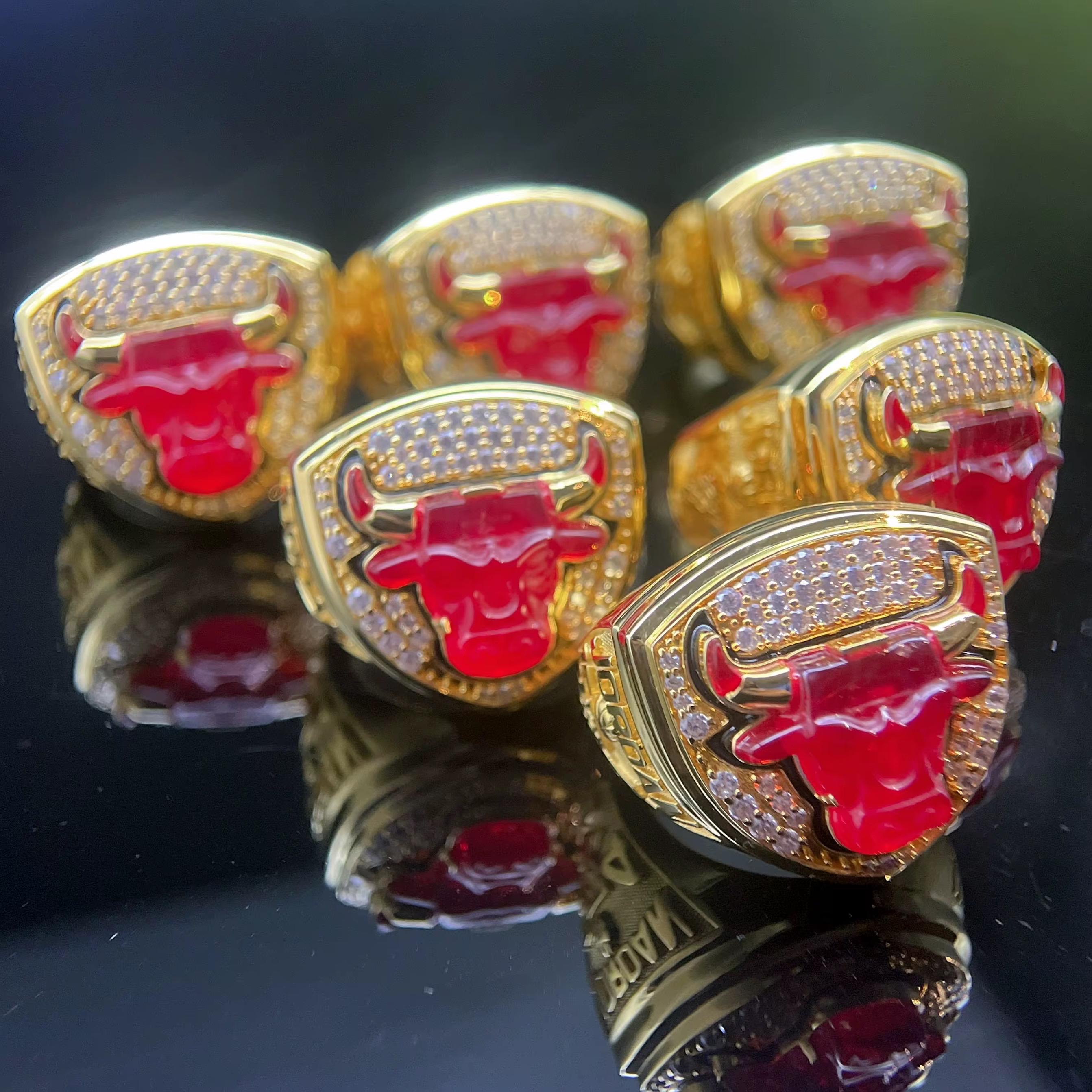 Set of championship rings with a prominent red bull logo on a reflective surface.