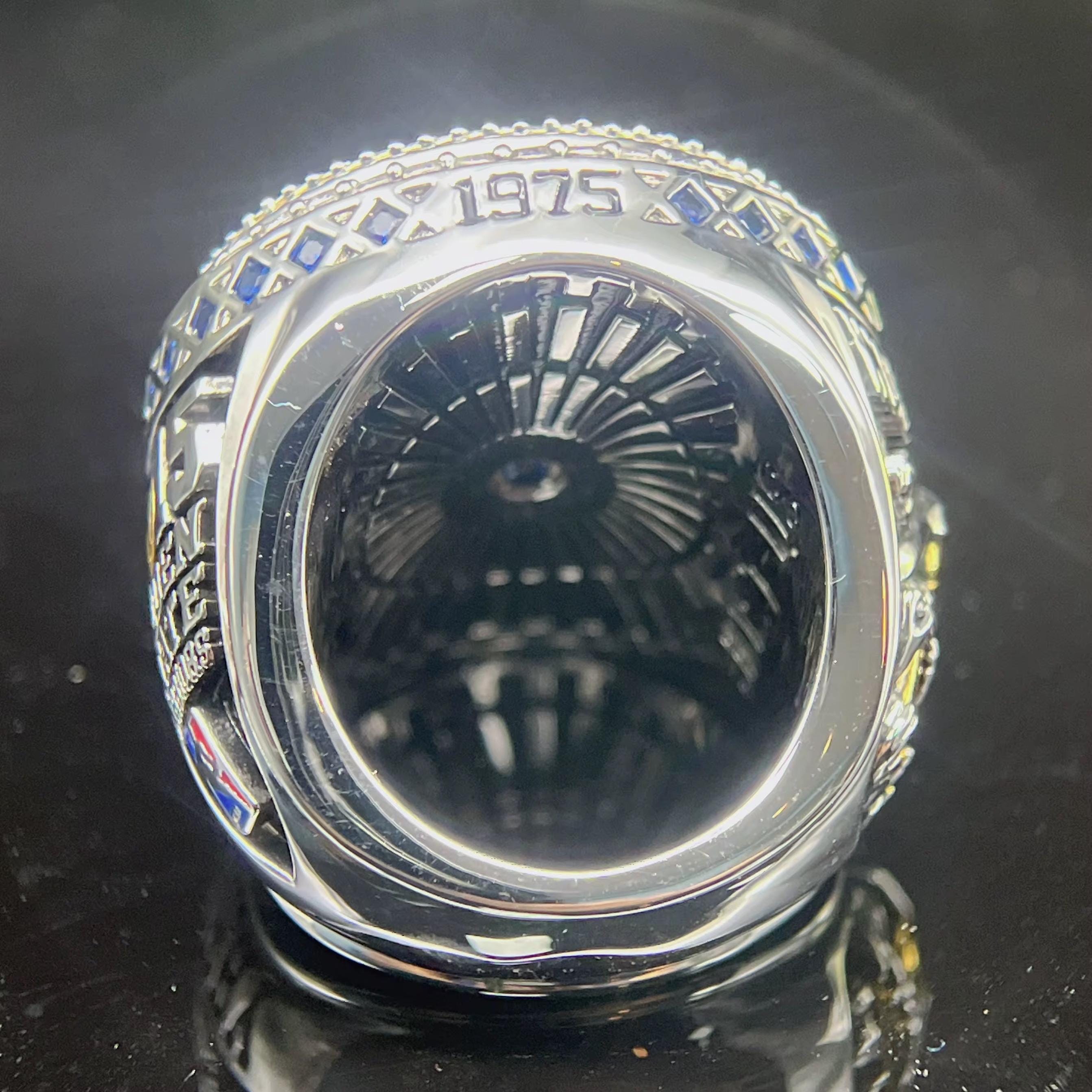 Silver ring with intricate design and '1975' engraving on a reflective black surface