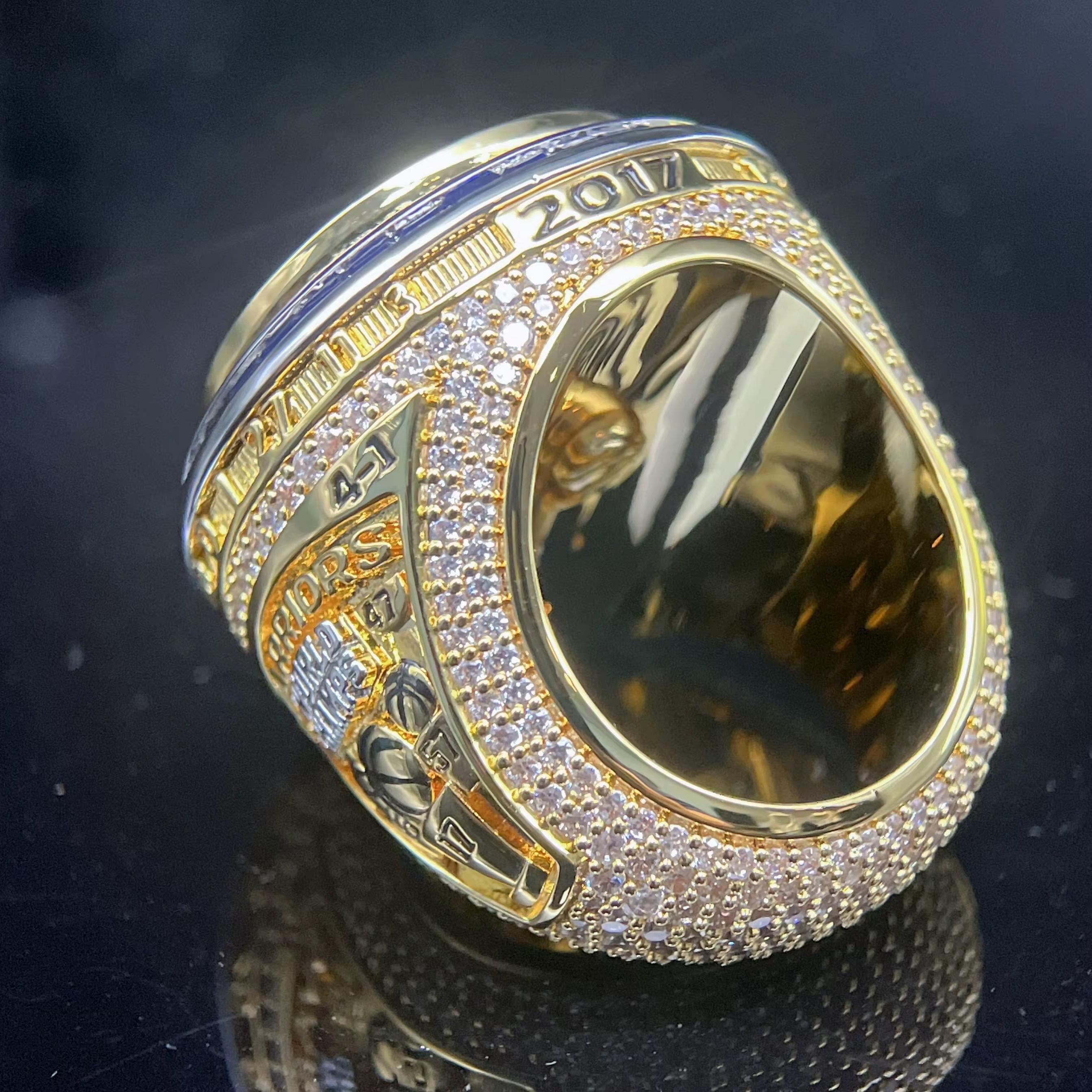 Gold ring with diamonds and text on a reflective surface