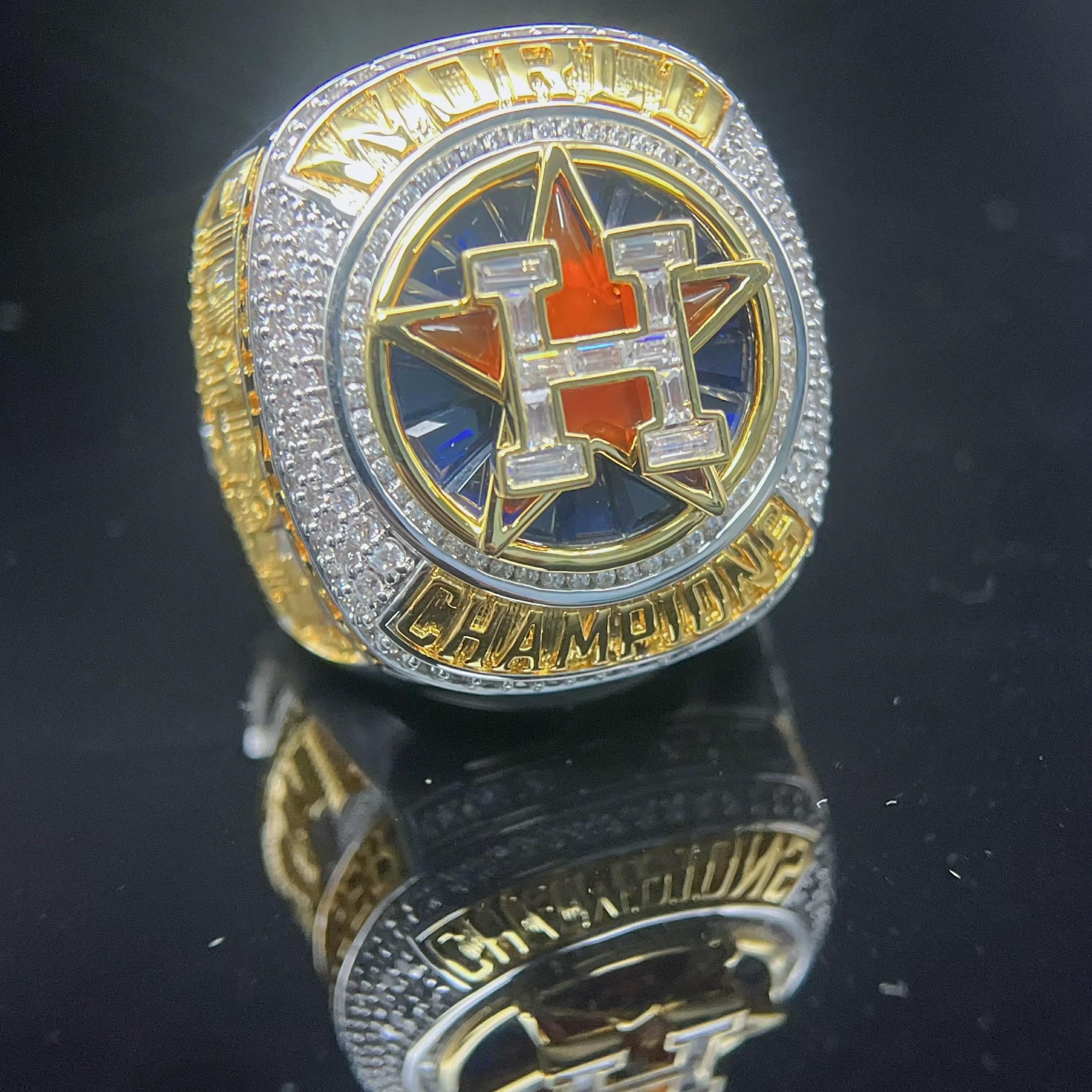 Metallic championship ring with 'H' logo on a reflective black surface