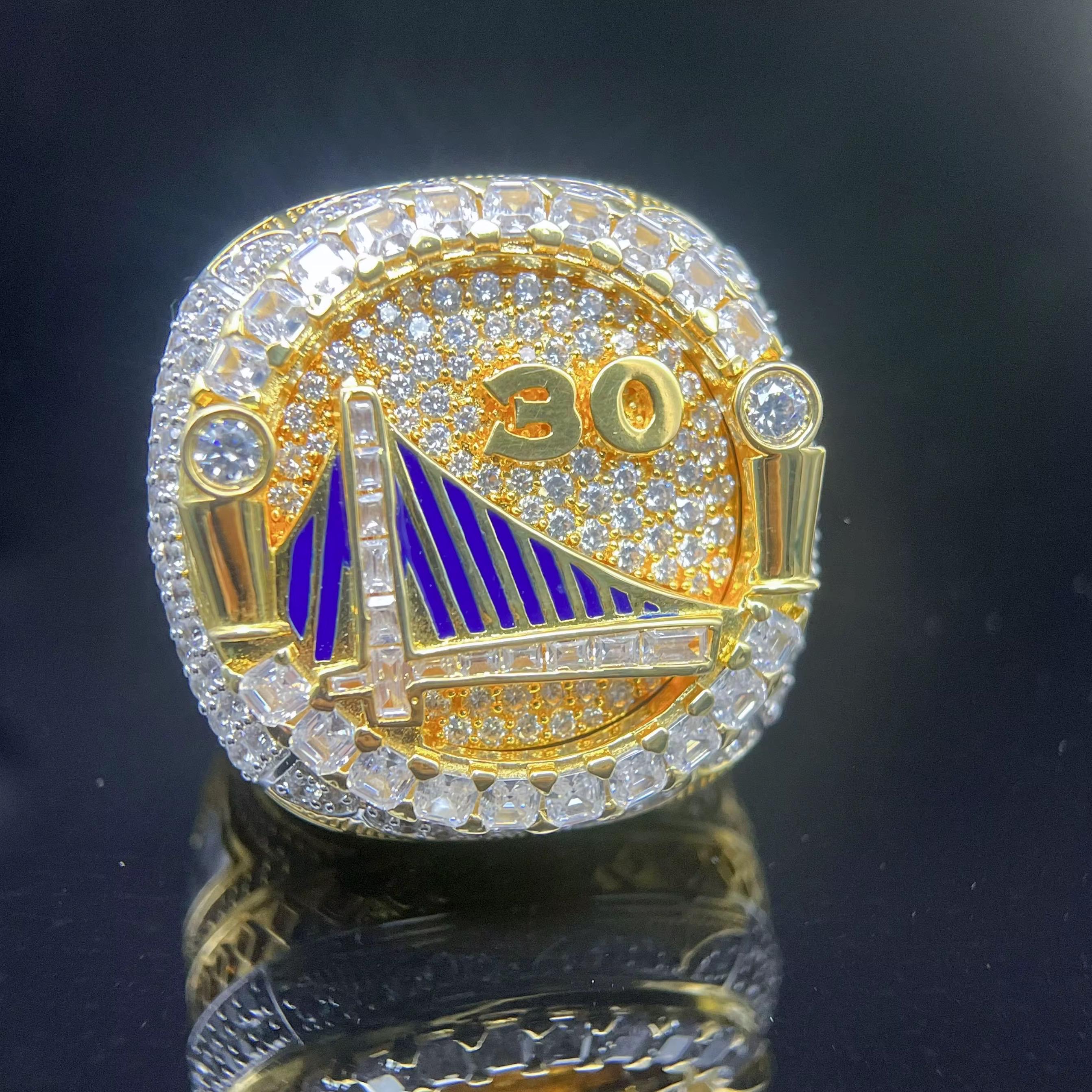 Gold and diamond-encrusted ring with '30' and sailboat design on a dark background