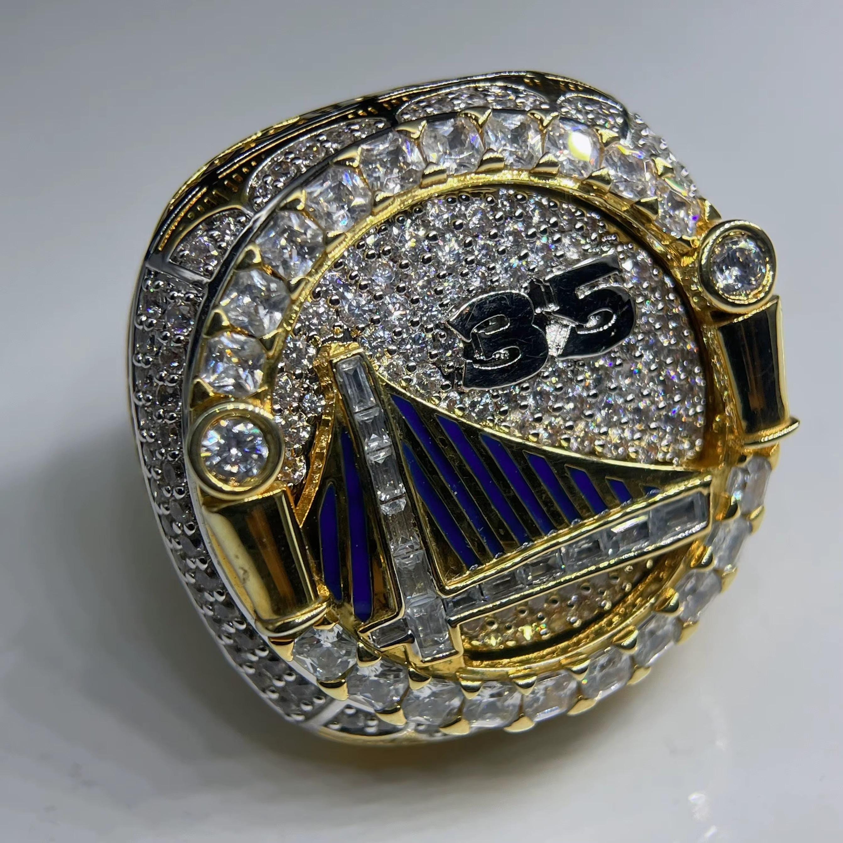 Gold and diamond-encrusted ring with a number 85 and blue emblem on a white background