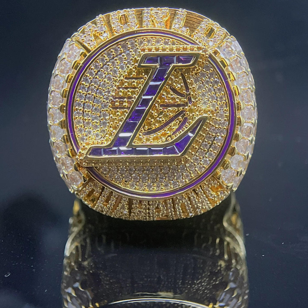 Gold ring with a prominent 'L' symbol on a reflective surface
