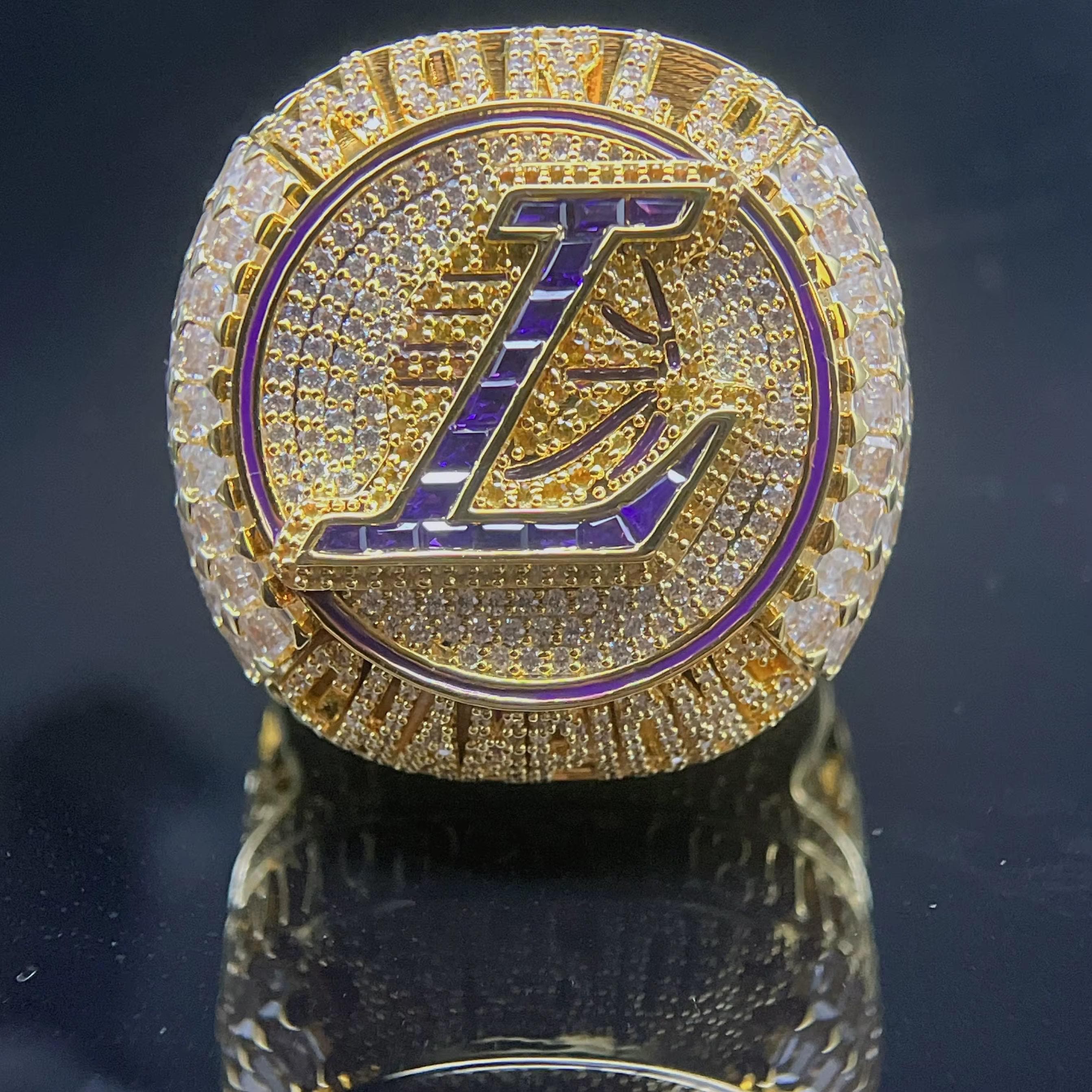 Gold ring with a prominent 'L' symbol on a reflective surface