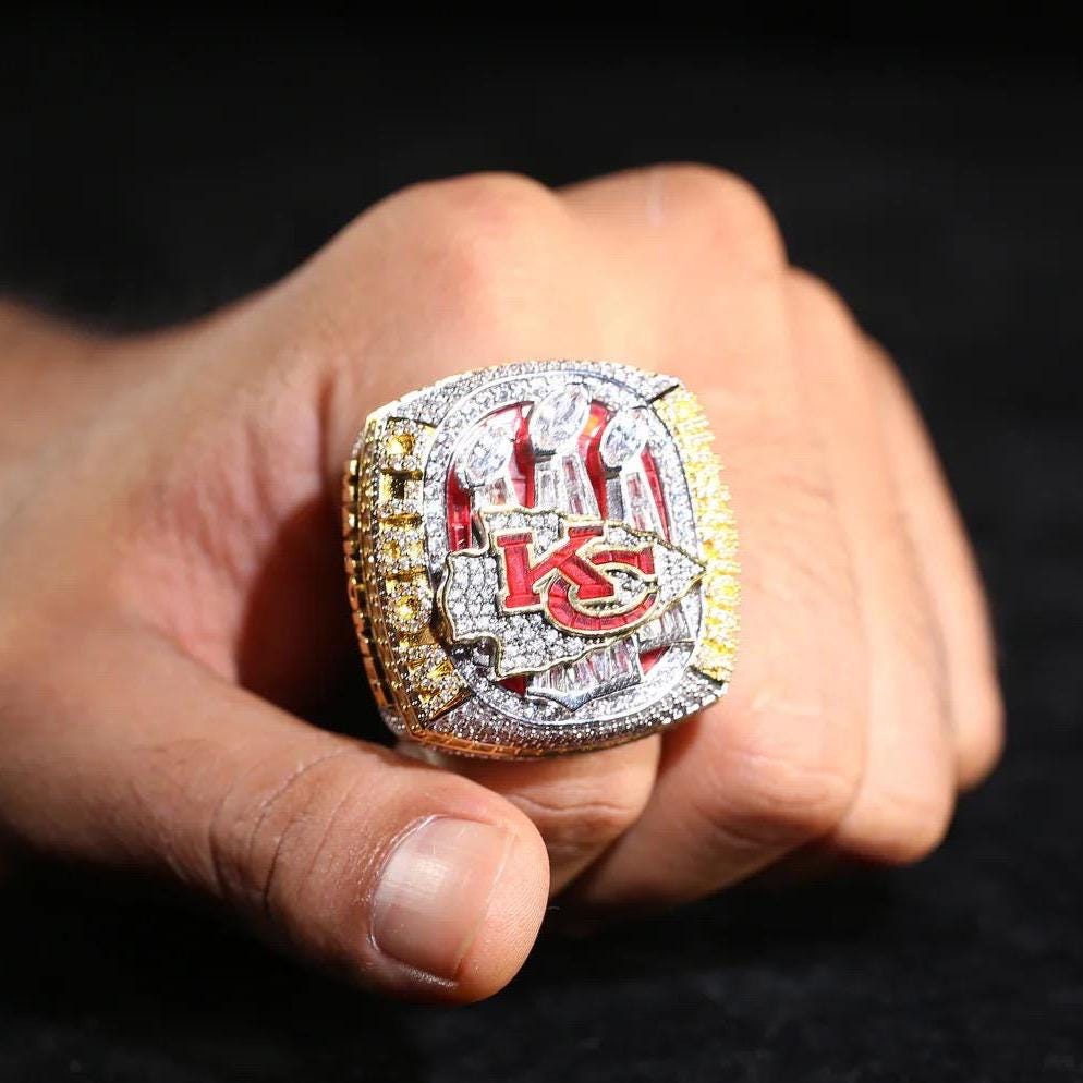 Close-up of a hand holding a championship ring with 'KC' logo on a dark background