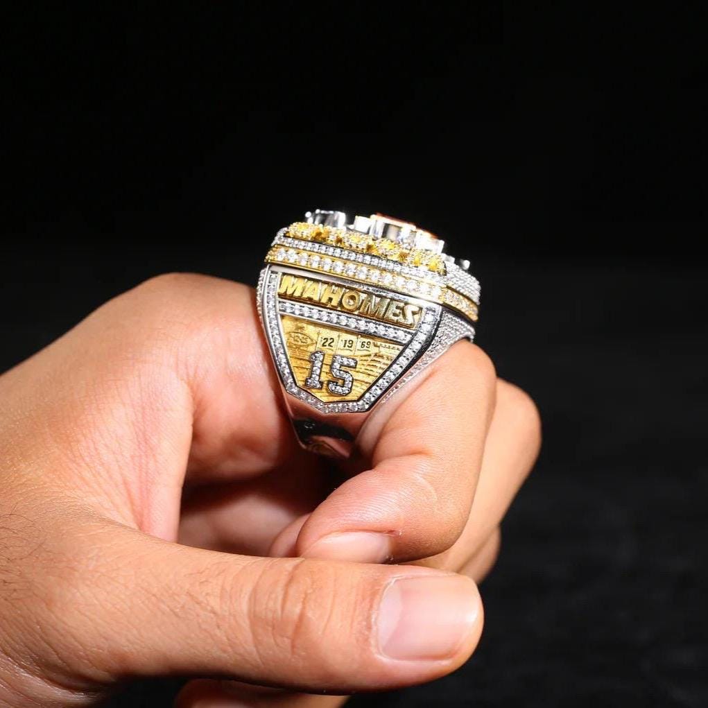 Hand holding a championship ring with 'Mahomes' and 'Super Bowl' text on a black background