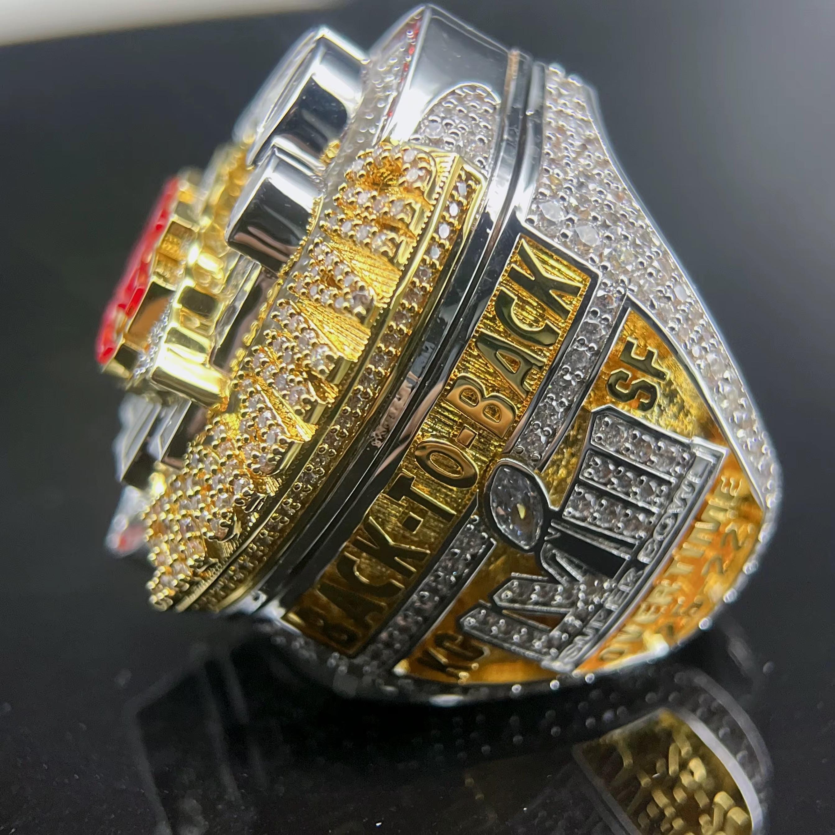 Close-up of a gold and silver championship ring with text on a reflective surface.