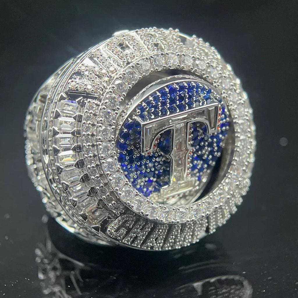 Silver ring with blue gemstone and 'T' emblem on a black background