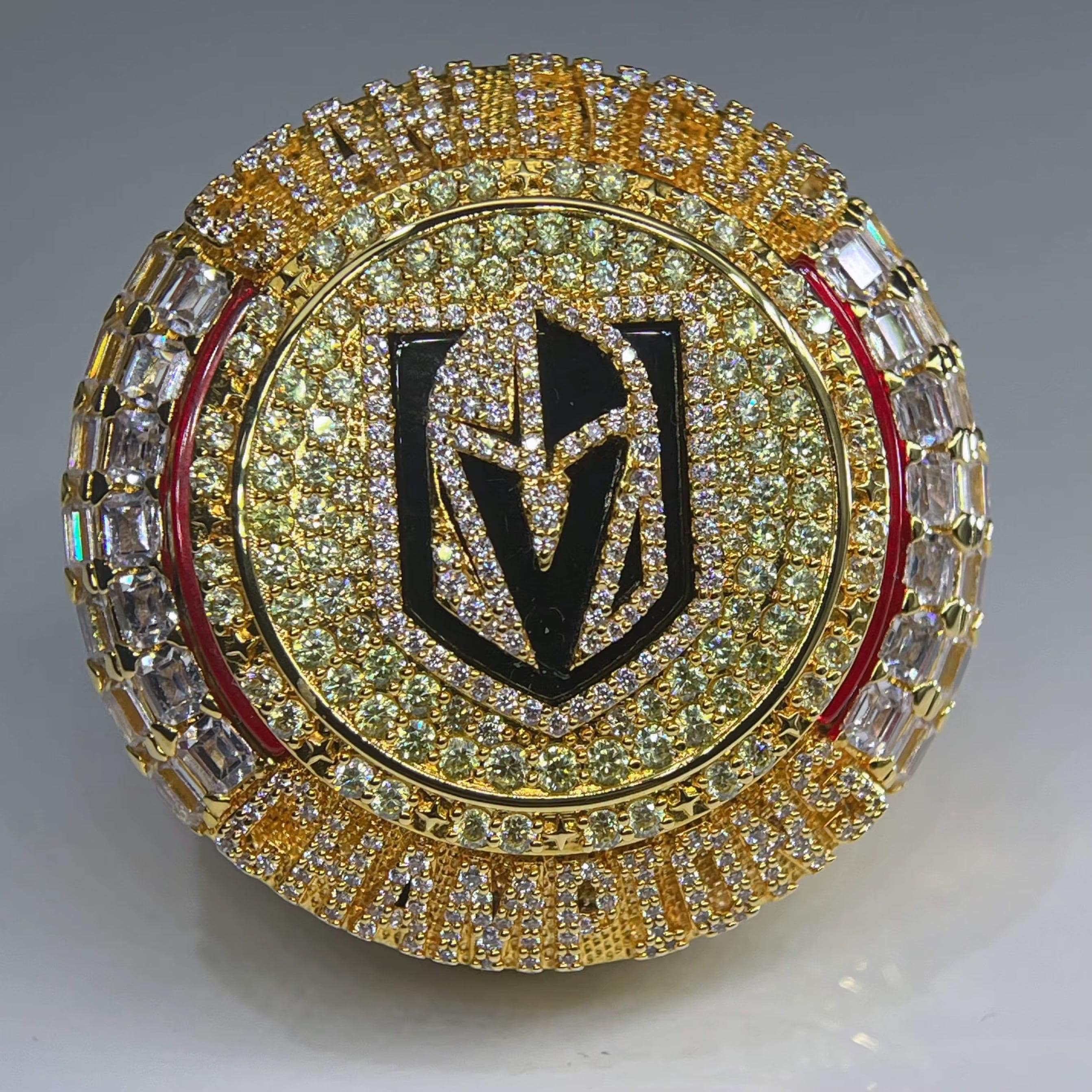 Gold and diamond-encrusted ring with a prominent logo on a gray background